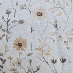 May include: A woven fabric featuring a repeating botanical print of wildflowers and delicate stems in shades of muted beige, soft brown, and cream. The textile displays a visible cross-hatch weave pattern throughout the entire surface area.