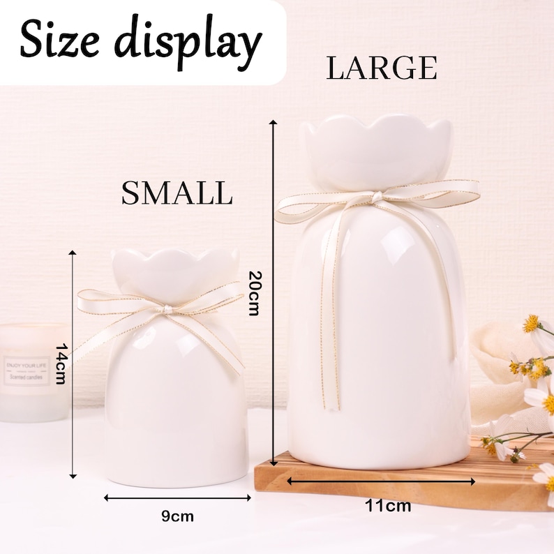 May include: Two white ceramic vases, one small and one large, with a flower-shaped top and tied with a ribbon. The small vase is 14cm tall and 9cm wide, while the large vase is 20cm tall and 11cm wide. The text "Size display" is at the top.