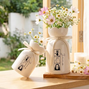 May include: A white ceramic mug with a black handle and the text "But First, Coffee" in a black, handwritten-style font. The mug is on a white surface.
