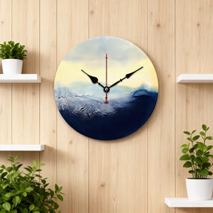 May include: Round wall clock with a painted abstract design in shades of blue, yellow, and white. The clock has black hands and a red second hand. The clock is mounted on a wooden wall.