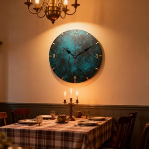 May include: A round wall clock with a teal and black textured face hangs on a beige wall. The clock has gold-colored hands and hour markers. The clock is above a dining table set for a meal.