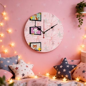 May include: A round wall clock with a pink background and a starburst pattern. The clock face features three framed cartoon animals: a cat, a fox, and another cat. The clock has black hands and a red second hand. The clock is hanging on a pink wall.