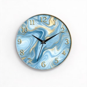 Puede incluir: Reloj de pared redondo con diseño de mármol azul y dorado. La esfera del reloj presenta números dorados y manecillas negras. El reloj tiene un marco metálico dorado.