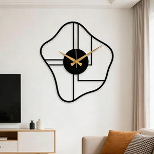 Puede incluir: Un reloj de pared moderno con un marco negro abstracto y una esfera circular negra. Las manecillas del reloj son doradas. El reloj está montado en una pared blanca, agregando un toque contemporáneo a la decoración de la habitación.