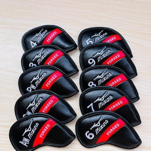 Puede incluir: Un conjunto de fundas negras para palos de golf con rayas rojas y texto bordado en blanco. Cada funda está etiquetada con un número o letras, y el logotipo de Mizuno es visible.