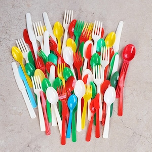 Puede incluir: Una colección de cubiertos de plástico de colores, que incluye cucharas, tenedores y cuchillos. Los utensilios son de varios colores como rojo, verde, amarillo, blanco y azul. La disposición está dispersa sobre una superficie neutra.