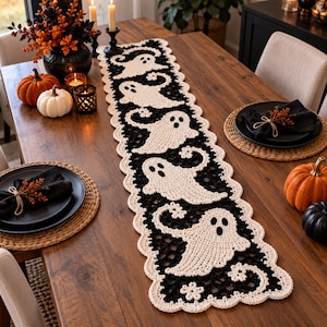 Peut inclure: Un chemin de table rectangulaire en crochet présentant un motif répétitif de fantômes couleur crème sur un fond noir avec une bordure festonnée crème. Le chemin est centré sur une table en bois, mettant en valeur le travail du fil.