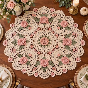 May include: A round, cream-colored crochet doily featuring an intricate lace pattern with raised, three-dimensional pink floral motifs and sage green leaves arranged in a symmetrical, radial design across the entire surface of the textile.