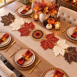 May include: A crochet table runner featuring a series of interconnected maple leaves in shades of brown, cream, and red, centred with a circular floral motif. The runner is displayed on a wooden dining table with place settings and autumn decor.