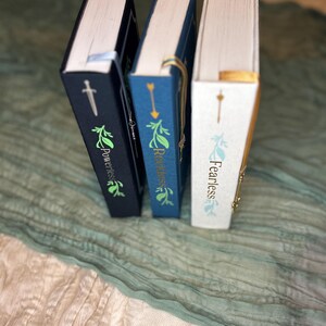 May include: Three hardcover books with decorative covers. The books are in navy blue, blue, and white. Each book has gold lettering and a decorative design. The spines display the titles "Powerless", "Reckless", and "Fearless". Each book has a ribbon bookmark.