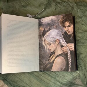 May include: Open book with a detailed illustration of a woman with white hair having her braid done by a man. The illustration is in grayscale with a soft, painterly style. The left page has printed text.