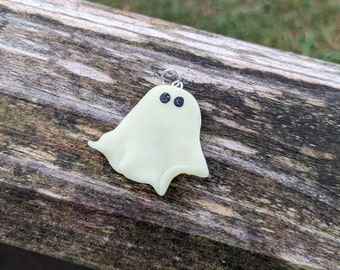 May include: A small, white, glow-in-the-dark ghost charm with black eyes. The charm is made of polymer clay and has a loop for hanging.