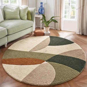 Puede incluir: Una alfombra redonda con un patrón geométrico en tonos beige, marrón y verde. La alfombra está hecha de un material suave y afelpado, diseñada para agregar calidez y estilo a cualquier espacio habitable. Diámetro aproximado de 200 cm.