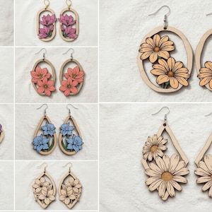 May include: A selection of wooden earrings with floral designs. The earrings feature various shapes, including teardrops and ovals, and are adorned with painted flowers in shades of pink, orange, purple, blue, and cream. Each pair has a silver hook.