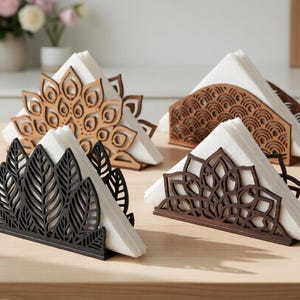 Pode incluir: Quatro porta-guardanapos decorativos de madeira em vários designs. Um é castanho claro com um padrão de mandala, outro é castanho escuro com um padrão geométrico, um terceiro é preto com um design de folhas e o último é castanho escuro com um design floral.