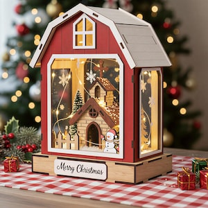 May include: A red and white wooden barn-shaped lantern featuring a miniature church scene inside with a snowman, a small tree, and warm string lights. The base has a white plaque with the text Merry Christmas in black script lettering.