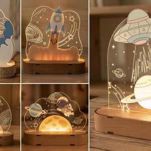 May include: A collection of decorative LED night lights with space-themed designs. Each light features a wooden base and a laser-cut acrylic design depicting astronauts, rockets, planets, and a UFO. The lights emit a warm glow, creating a whimsical ambiance.