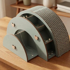 May include: A sage green wooden jewelry organizer with a semi-circular arch design. It features a pull-out drawer with a small circular knob, open shelving compartments for rings and earrings, and a textured, patterned side panel with a grid design.
