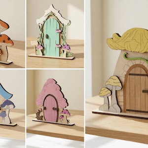 Peut inclure: Collection de cinq décorations de portes de fées en bois. Chaque porte présente un design unique, avec des toits en forme de champignon, des portes cintrées et des accents colorés. Les portes sont posées sur une surface en bois.