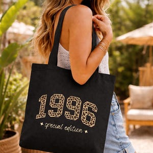 Könnte beinhalten: Schwarze Tragetasche mit der Jahreszahl "1996" im Leopardenmuster. Darunter steht "special edition". Die Tasche hat lange schwarze Henkel.