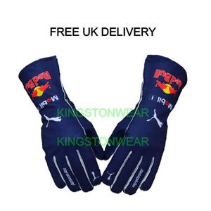 Peut inclure: Une paire de gants de course bleu marine avec des détails blancs. Les gants présentent le logo Red Bull en rouge et jaune, ainsi que le logo Mobil 1. Le logo Puma est également visible en blanc.