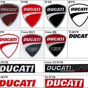 Peut inclure: Une collection d'écussons brodés présentant le logo Ducati sous diverses formes de boucliers et de rectangles. Les motifs incluent des couleurs rouge, blanc, noir et carbone avec le texte DUCATI et CORSE affiché en différentes combinaisons.
