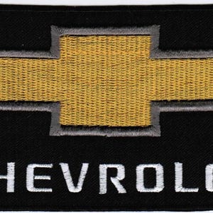 May include: A rectangular black embroidered patch featuring the gold Chevrolet bowtie logo centered at the top. Below the logo, the word CHEVROLET is stitched in white capital letters. The entire design is set against a solid black fabric background.