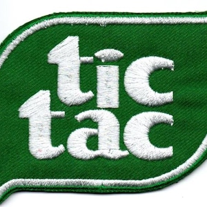 Peut inclure: Un écusson brodé vert en forme de feuille arrondie ou de bulle de dialogue avec le texte blanc tic tac en minuscules. L'écusson présente une bordure épaisse cousue en blanc qui souligne toute la forme de la base en tissu vert.