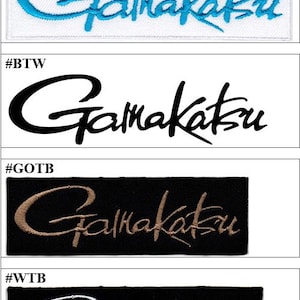 May include: A collection of four rectangular embroidered patches featuring the brand name Gamakatsu in a stylised script font. The patches include a white background with blue text, a white background with black text, a black background with gold text, and a black background with white text.