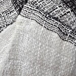 Puede incluir: Un tejido textil con un patr&oacute;n de tejido suelto y abierto. El material muestra un marcado contraste entre una secci&oacute;n blanca s&oacute;lida y una secci&oacute;n con un patr&oacute;n de cuadros en blanco y negro. Las fibras se ven suaves y ligeramente texturizadas.
