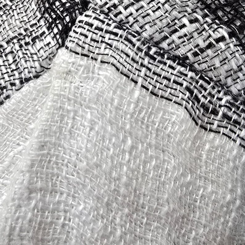 Puede incluir: Un tejido textil con un patr&oacute;n de tejido suelto y abierto. El material muestra un marcado contraste entre una secci&oacute;n blanca s&oacute;lida y una secci&oacute;n con un patr&oacute;n de cuadros en blanco y negro. Las fibras se ven suaves y ligeramente texturizadas.