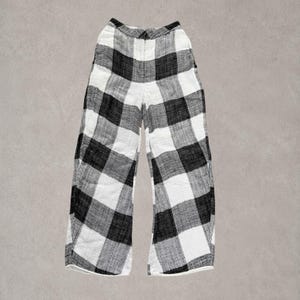 Puede incluir: Pantalones de talle alto con un llamativo estampado de cuadros negros y blancos. Estos pantalones de pernera ancha cuentan con una cintura estructurada con cierre de bot&oacute;n frontal y una silueta recta y relajada hasta los tobillos.