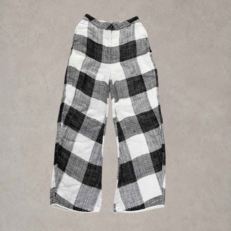 Puede incluir: Pantalones de talle alto con un llamativo estampado de cuadros negros y blancos. Estos pantalones de pernera ancha cuentan con una cintura estructurada con cierre de bot&oacute;n frontal y una silueta recta y relajada hasta los tobillos.