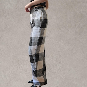 Puede incluir: Pantalones de talle alto con un llamativo estampado de cuadros en blanco y negro. Los pantalones presentan un corte recto, una cintura estructurada con cierre de bot&oacute;n y un bolsillo lateral visible. La tela tiene un aspecto texturizado.