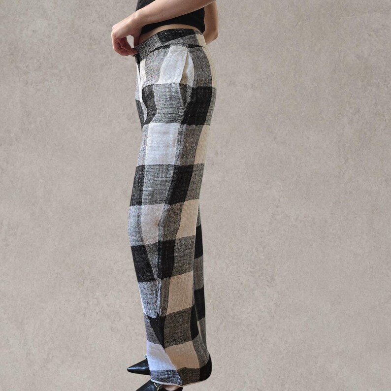 Puede incluir: Pantalones de talle alto con un llamativo estampado de cuadros en blanco y negro. Los pantalones presentan un corte recto, una cintura estructurada con cierre de bot&oacute;n y un bolsillo lateral visible. La tela tiene un aspecto texturizado.