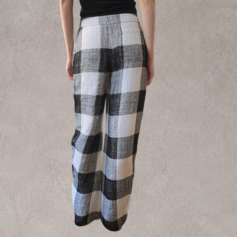 Puede incluir: Pantalones largos con un llamativo patr&oacute;n de cuadros en blanco y negro. Estos pantalones de pierna ancha est&aacute;n confeccionados con un ajuste de cintura alta y un acabado de tela texturizada, mostrando un dise&ntilde;o de cuadr&iacute;cula desde la cintura al dobladillo.