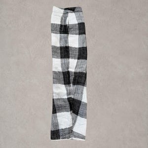 Puede incluir: Un pantal&oacute;n con un patr&oacute;n de cuadros grandes en blanco y negro. La prenda presenta una silueta de pierna recta con una cintura visible y un detalle de costura lateral, mostrando una textura tejida en toda la estructura de la tela.