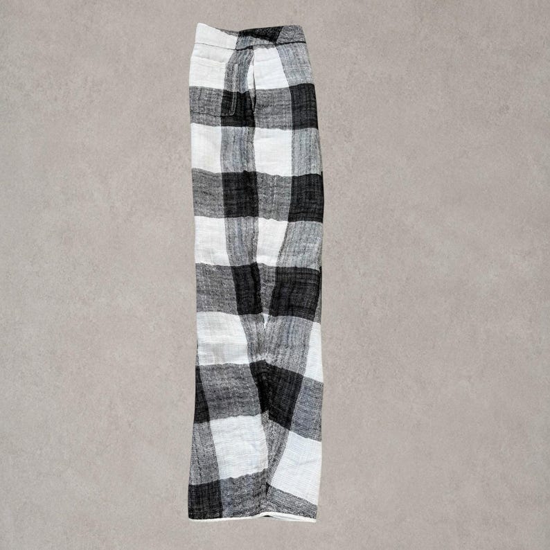 Puede incluir: Un pantal&oacute;n con un patr&oacute;n de cuadros grandes en blanco y negro. La prenda presenta una silueta de pierna recta con una cintura visible y un detalle de costura lateral, mostrando una textura tejida en toda la estructura de la tela.
