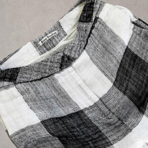Puede incluir: Un pantal&oacute;n con un patr&oacute;n de cuadros en blanco y negro con un acabado de tela tejida texturizada. La cintura incluye una etiqueta interior blanca con el texto negro Acne Studios impreso, visible en el borde superior de la prenda.