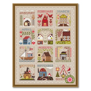 May include: A framed cross-stitch sampler featuring twelve seasonal house designs, each representing a month. The artwork includes houses, boats, and nature elements, with text indicating the months. The frame is a warm brown color.
