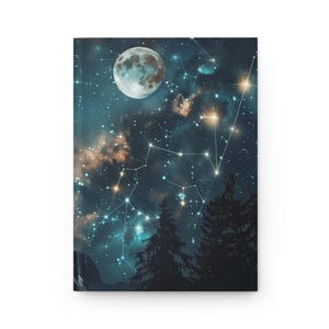 May include: A rectangular hardcover journal featuring a dark blue night sky illustration with a large full moon, scattered bright stars, and connected constellations. The bottom of the cover shows the dark silhouettes of tall pine trees.