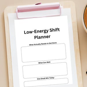 May include: A white planner titled "Low-Energy Shift Planner" with sections for "What Actually Needs to Get Done", "What Can Wait", and "One Small Win Today". The planner is held by a pink clip on a wooden clipboard.