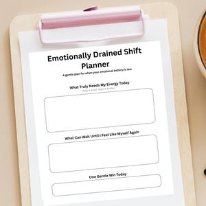 May include: A white planner with a pink clip, titled "Emotionally Drained Shift Planner." The planner features prompts: "What Truly Needs My Energy Today," "What Can Wait Until I Feel Like Myself Again," and "One Gentle Win Today."