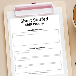 Może przedstawiać: Biały papierowy planista zmian zatytułowany "Short Staffed Shift Planner" przypięty do jasnoróżowej tablicy. Planista zawiera sekcje dotyczące skupienia, zadań priorytetowych i działań.