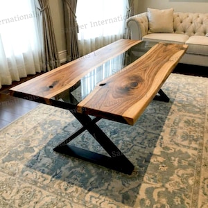 Puede incluir: Una mesa de madera moderna con borde natural y centro de resina epoxi transparente. La mesa presenta un patrón de vetas de madera natural y está sostenida por patas cruzadas de metal negro. Una pieza llamativa para salón o comedor, de unos 200 cm de largo.