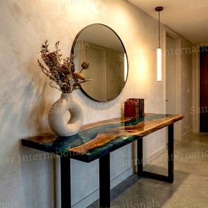 May include: A modern console table with a live edge wooden top inlaid with blue and green resin. The table has black metal legs and is decorated with a white vase, dried flowers, and a round mirror.