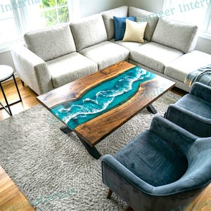 May include: A rectangular coffee table featuring a natural wood slab with a central river design made of turquoise resin and white foam accents. The table has black metal legs and is positioned on a gray rug in front of a light gray sectional sofa.