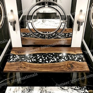 May include: A modern wooden bench with a black and white speckled inlay. The bench has a natural wood grain finish and is supported by silver metal legs. A large circular mirror hangs above the bench.