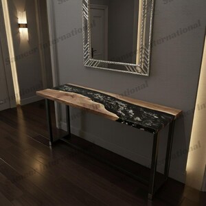 May include: A wooden console table with a black epoxy river design. The table has a natural wood edge and sits on a black metal frame. A mirror hangs on the wall behind the table.