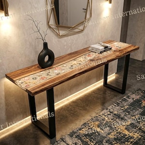 May include: A rectangular console table with a natural wood grain top featuring a central resin inlay filled with seashells and starfish. The table has black metal U-shaped legs and supports a black ceramic vase with a branch and a stack of books.